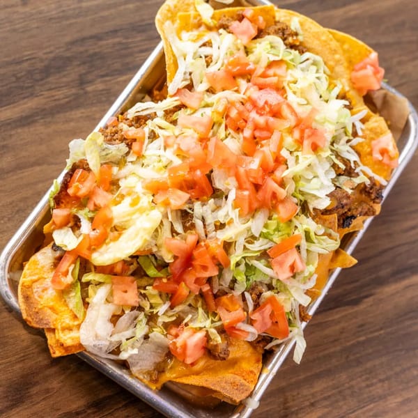 A metal tray filled with nachos topped with ground beef, shredded lettuce, and diced tomatoes.