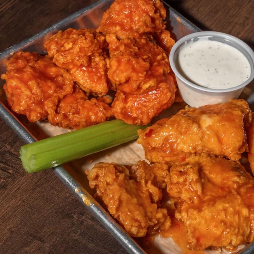 Buffalo chicken wings with celery and ranch dressing on a metal tray.