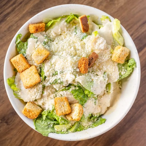 Overhead view of a Caesar salad with romaine lettuce, dressing, croutons, and grated cheese.