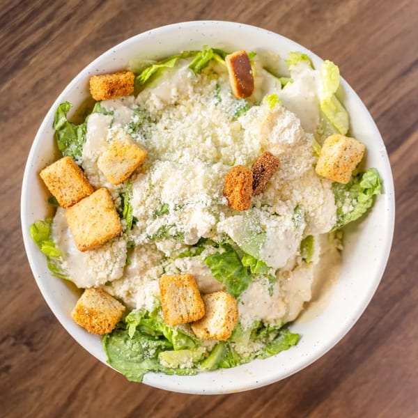 Overhead view of a Caesar salad with romaine lettuce, dressing, croutons, and grated cheese.
