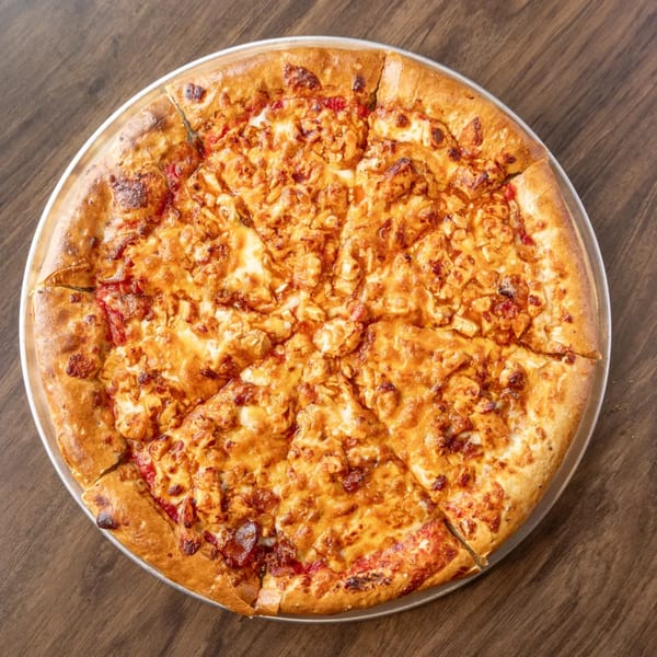 A whole, sliced chicken pizza with a golden crust sits on a metal pan atop a wooden table.