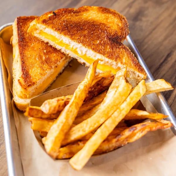 Golden grilled cheese sandwich cut in half, served with a side of crispy french fries on a metal tray.