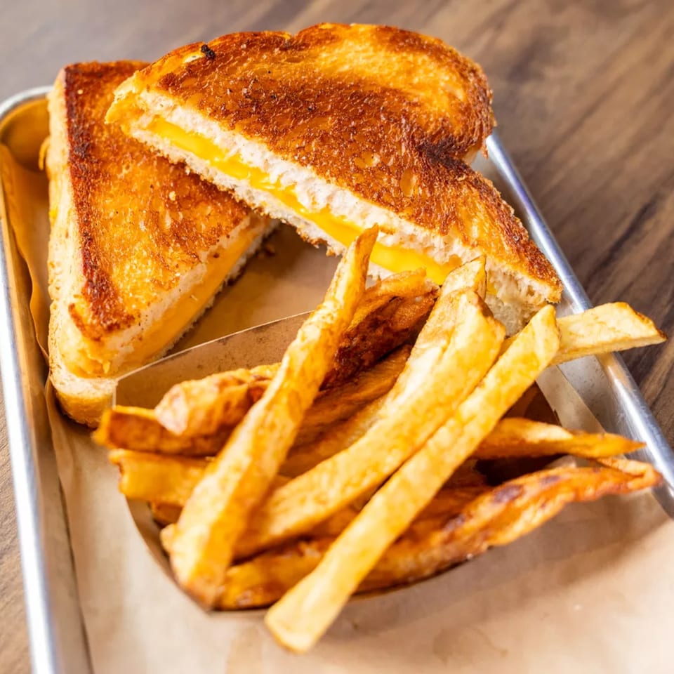 Golden grilled cheese sandwich cut in half, served with a side of crispy french fries on a metal tray.