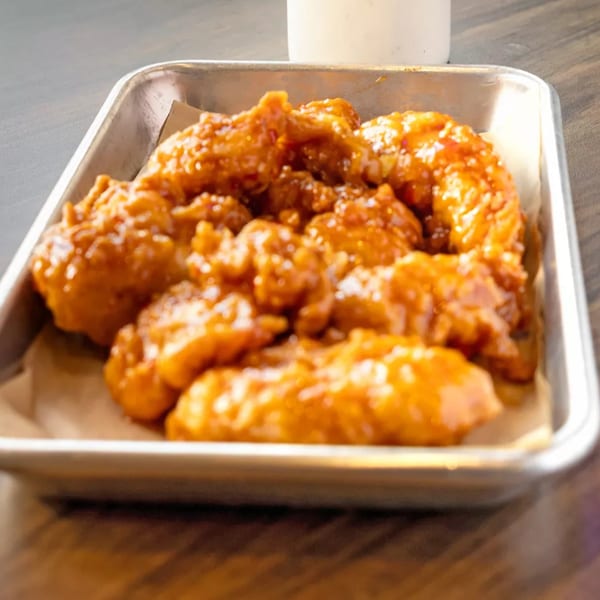 Crispy, golden-brown chicken tenders coated in a sweet and savory sauce, served in a metal tray.