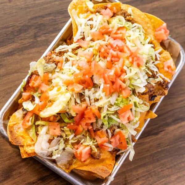 A metal tray filled with loaded nachos topped with ground beef, shredded lettuce, and diced tomatoes.