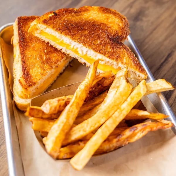 Golden grilled cheese sandwich cut in half, served with a side of crispy french fries on a metal tray.