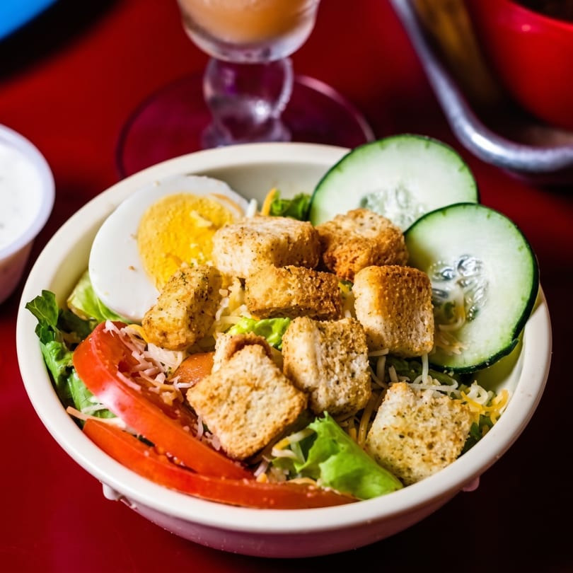 A vibrant salad with lettuce, tomatoes, cucumbers, croutons, cheese, and a hard-boiled egg.