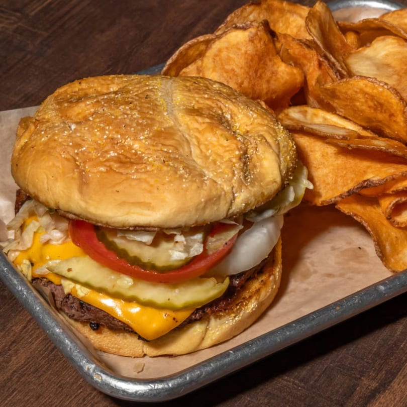 Cheeseburger with lettuce, tomato, onion, pickles, and a side of crispy potato chips.