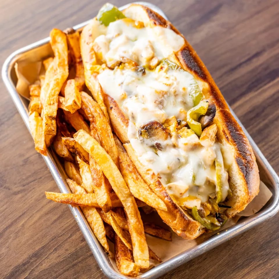 Cheesesteak sandwich with melted cheese, peppers, and onions, served with a side of fries.