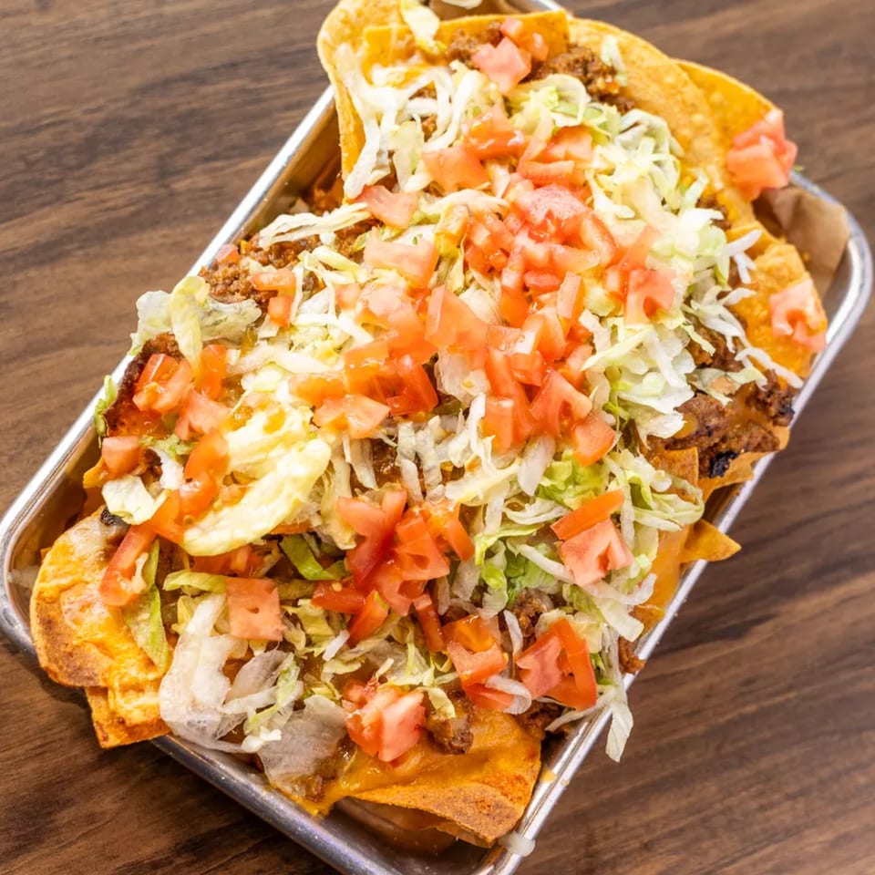 Loaded nachos with ground beef, shredded lettuce, and diced tomatoes in a metal tray.