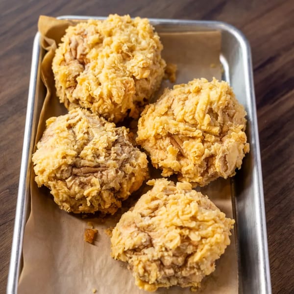 Four pieces of crispy fried chicken on parchment paper in a metal tray.