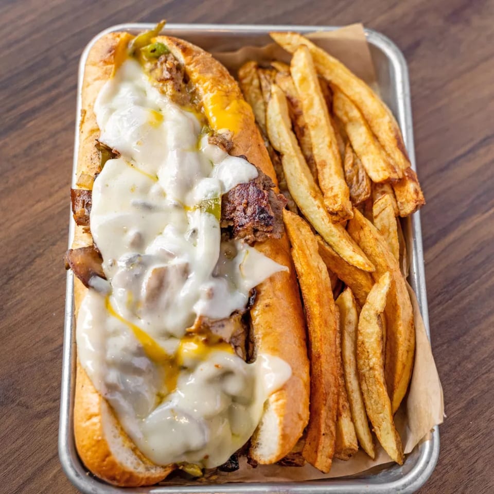 Cheesesteak sandwich with melted cheese and green peppers, served with a side of french fries.