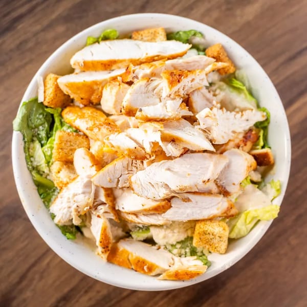 Overhead view of a Caesar salad with grilled chicken, croutons, and dressing in a white bowl.