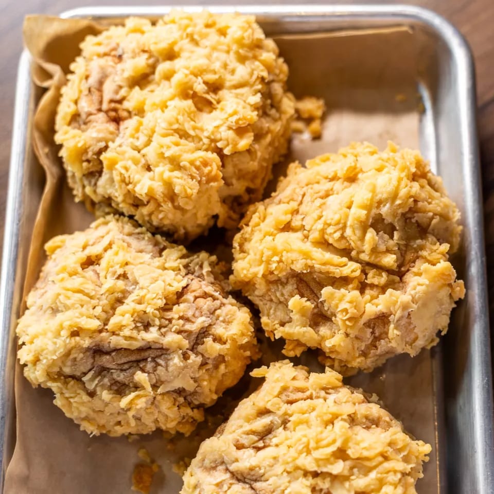 Four pieces of crispy fried chicken with golden-brown breading on a metal tray with parchment paper.
