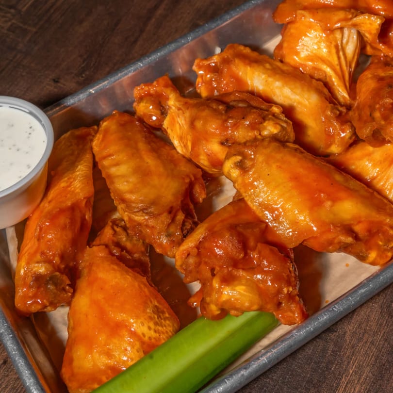 Buffalo wings with ranch dressing and celery sticks on a metal tray.