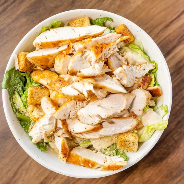 Overhead view of a Caesar salad with grilled chicken, croutons, and Parmesan cheese in a white bowl.